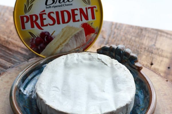 brie wheel A package of President Brie placed on top of a ceramic blue brie baking plate placed on a wooden board.