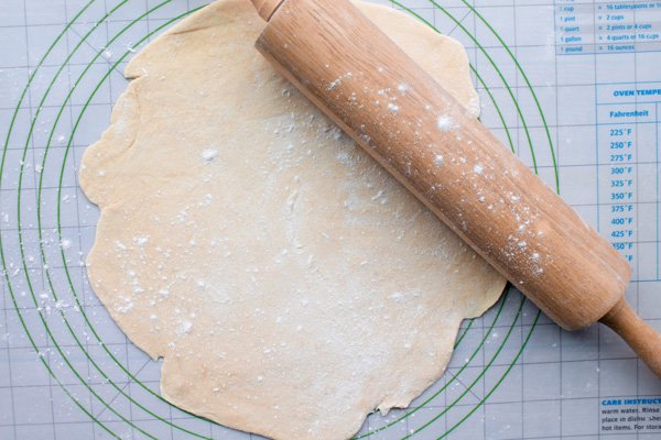 puff pastry Puff pastry dough being rolled out by a rolling pin into a circle placed on top of a pasty mat.