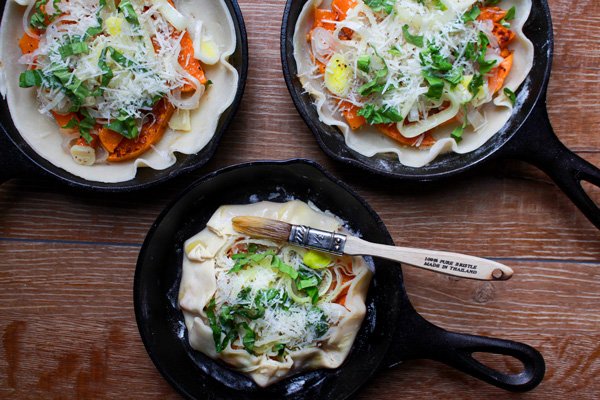butternut squash galettes Three mini cast iron skillets with prepared butternut squash galettes ready to be put in the oven placed on top of a wooden board.