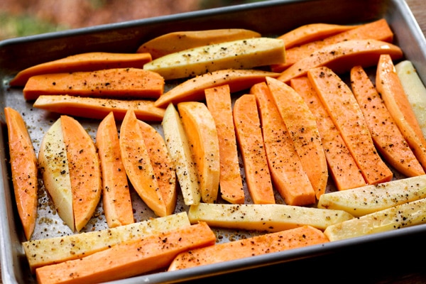 Sweet potatoes wedges placed on a baking sheet and sprinkled with spices read for the oven.