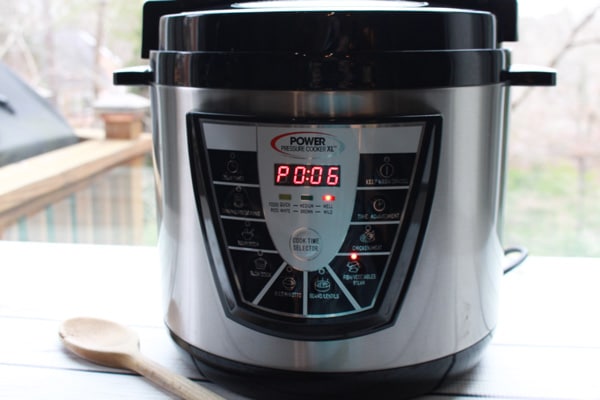 Power Pressure Cooker XL Instant Pot A pressure cooker instant pot placed on a white board with a wooden spoon on the side.