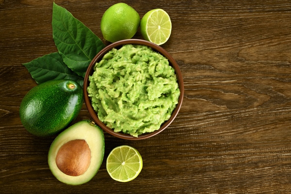 mashed avocados in a bowl with limes on the side on top of a wooden board.