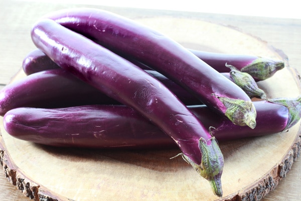 A pile of purple Chinese eggplant on top of a round wooden board.