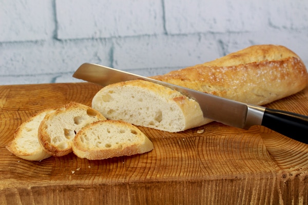 Sliced French bread French bread being sliced on a cutting board with a bread knife.