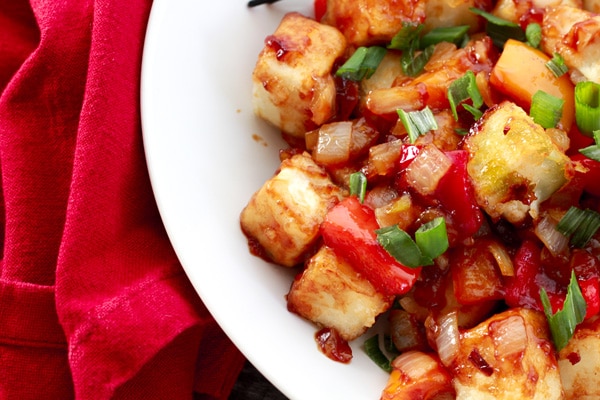 Healthy Vegetarian Sweet and Sour Tofu Crispy tofu cubes in a sweet and sour sauce in a white bowl with a red napkin on the side.