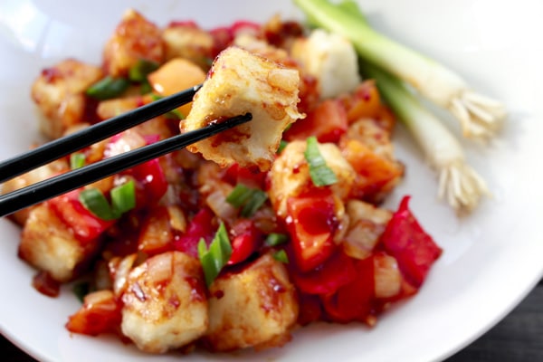 Healthy Vegetarian Sweet and Sour Tofu Crispy tofu cubes in a sweet and sour sauce in a white bowl with chopsticks on the side.