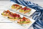 Sushi-grade salmon and tuna are nestled on top of avocado toast presented on a two white plates with a blue napkin on the side.
