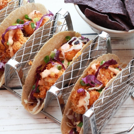 bang bang shrimp tacos in a taco holder with chips and a lime on the side.