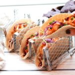 bang bang shrimp tacos in a taco holder with one taco hand held