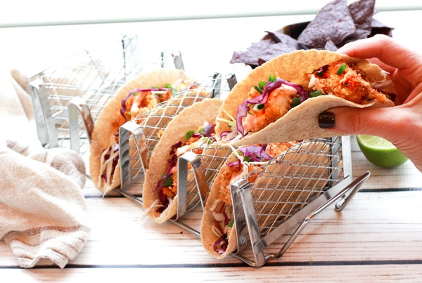 bang bang shrimp tacos in a taco holder and a taco held by hand.
