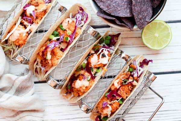 bang bang shrimp tacos in a taco holder with tortilla chips and lime on the side.