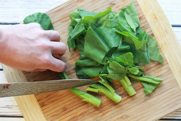 Chinese broccoli chopping Chinese broccoli on a wooden cutting board.