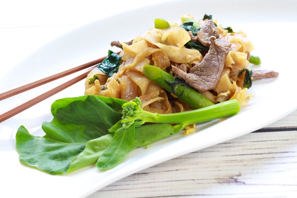 Thai Pad See Ew stir fried noodles on a plate with chopsticks and Chinese broccoli.