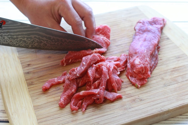sliced flank steak slicing flank steak on a wooden cutting board.