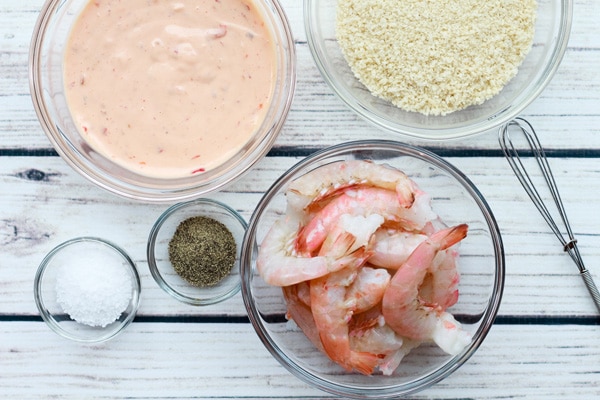 raw shrimp, panko breadcrumbs, spicy sauce, salt and pepper in glass bowls.