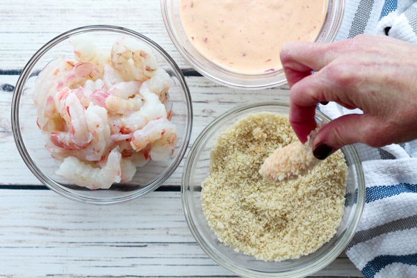 shrimp being dredged in Panko bread crumbs with spicy sauce in a glass bowl.
