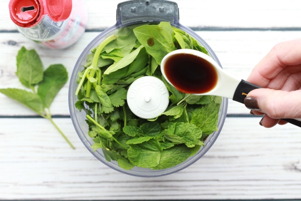 Fresh green herbs in a small food processor with a fish sauce pour.