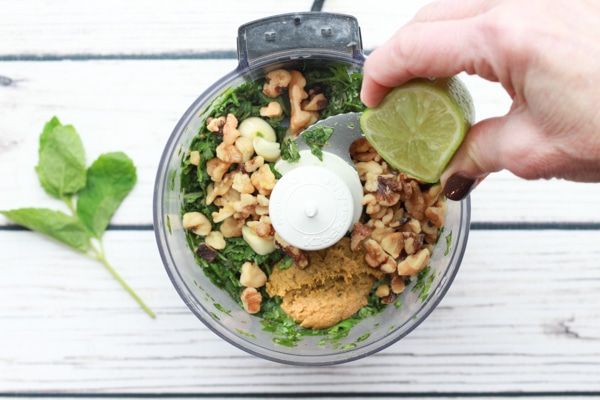 Fresh green herbs and nuts in a food processor ready to make a Thai pesto sauce with a squeeze of lime.