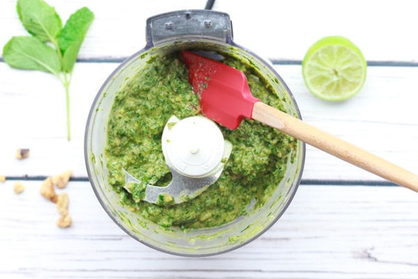 Thai basil pesto sauce in food processor with a rubber red spatula inserted.