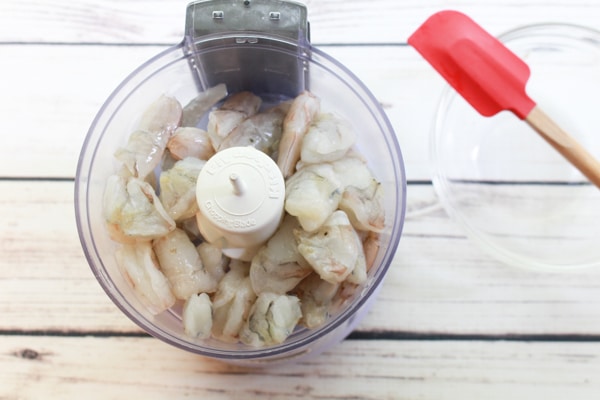 cut up shrimp inside a mini food processor ready to be chopped place on top of a white wooden board
