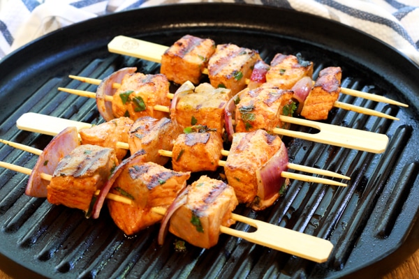 red curry salmon kebabs on wooden skewers being grilled on a grill pan