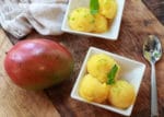 mango coconut sorbet in white bowls with a whole mango on the side