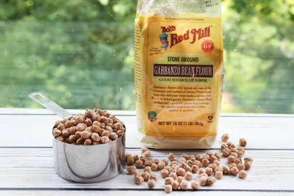 dried chickpeas in a measuring cup and garbanzo bean flour in a package on top of a wooden board