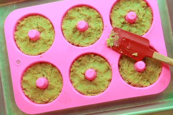 Matcha donut batter inside a pink silicone donut tray with a red spatula placed on top