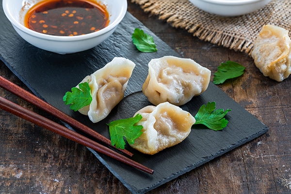 Chinese shrimp and pork dumplings - dim sum - on a black board with sweet chili dipping sauce and chopsticks on the side