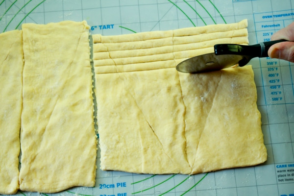 slicing pastry dough into thin strips with a pizza cutter on a dough mat