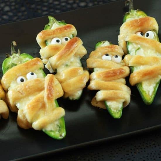 Halloween Jalapeño Poppers decorated like Mummies on a black plate