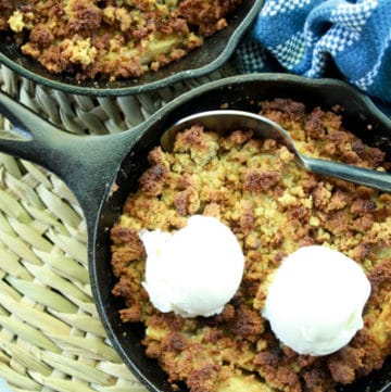Apple crisps topped with vanilla ice cream in mini cast iron skillets with a spoon and napkin on the side