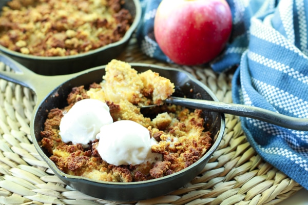 apple crisps topped with vanilla ice cream in mini cast iron skillets with a spoon and napkin on the side