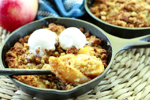 Apple crisps topped with vanilla ice cream in mini cast iron skillets with a spoon and napkin on the side