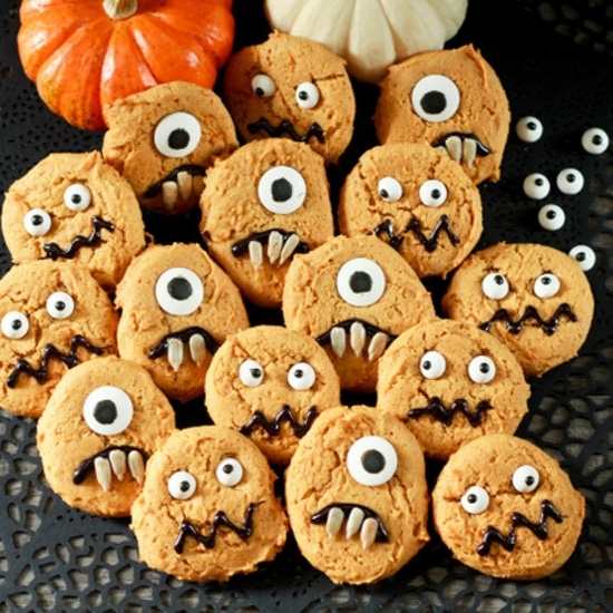 decorated pumpkin monster cookies on a black place mat with baby pumpkins on the side