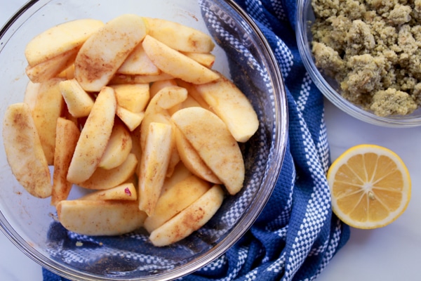 slices of apples in a glass bowl with apple crumble topping on the side