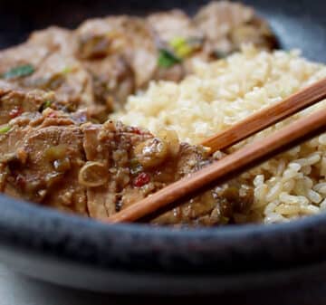 slices of pork tenderloin in a black bowl with a side of brown rice and wooden chopsticks