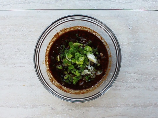 marinade for the pork tenderloin in a small glass bowl topped with green onions placed on top of a gray surface