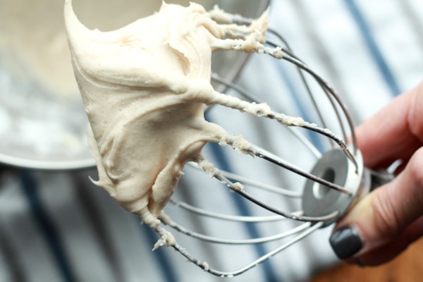 a woman holding a mixing whisk with a peak of whipped cream cheese frosting