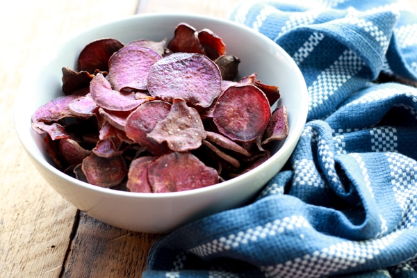 baked purple sweet potato chips in a white bowl with a blue napkin on the side