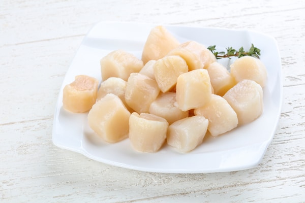 raw sea scallops on a white plate on a white wooden board