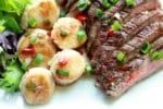 seared scallops and grilled flank steak on a white plate with a green salad on the side