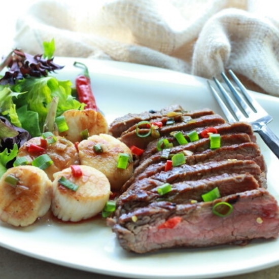 grilled flank steak slices and seared scallops on a white plate with a green salad on the side
