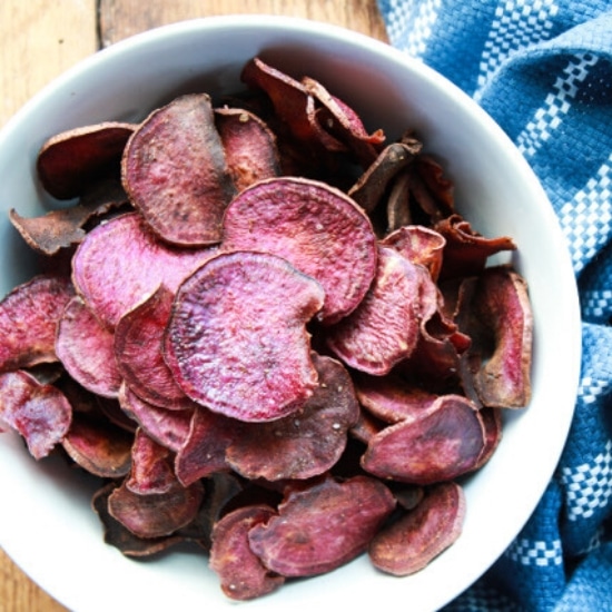 baked purple sweet potato chips in a white bowl with a blue napkin on the side