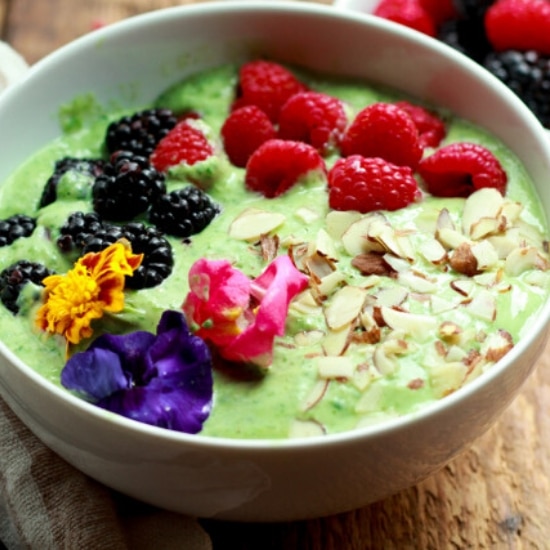 a green smoothie bowl topped with raspberries, blackberries, almonds and edible flowers