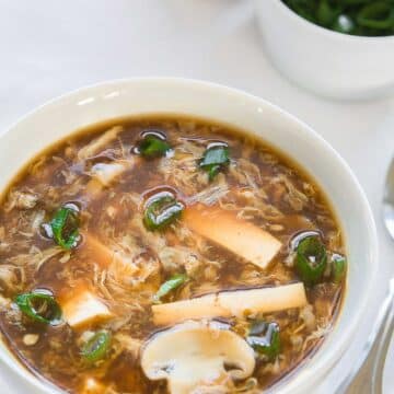 hot and sour soup in a white bowl with chopped green onions in the background