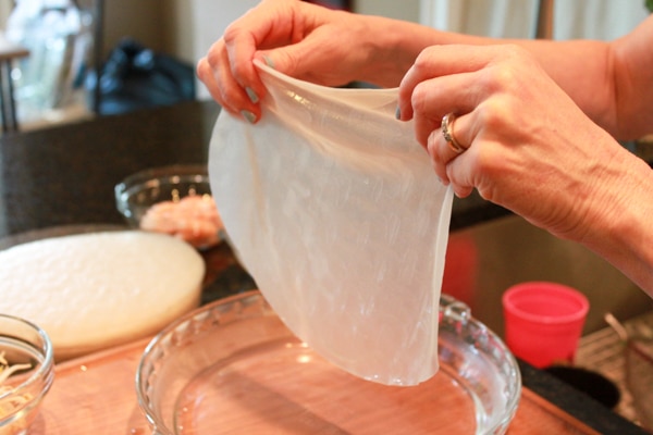 Hands holding up a rice paper wrapper that's been soaked in water.