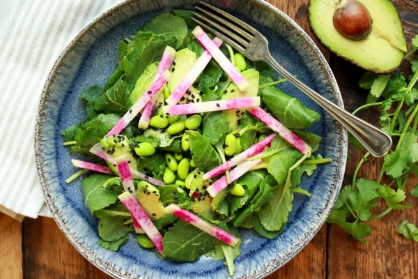 avocado-edamame kale salad in a blue bowl with a fork and avocado on the side