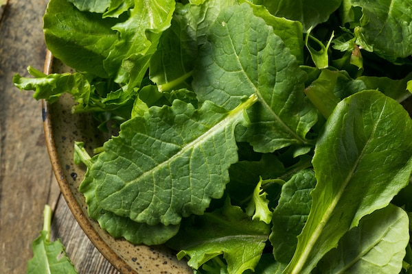 baby kale in a bowl on top of a wooden board