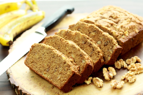 Sliced banana bread on a wooden board with walnuts and ripe bananas on the side